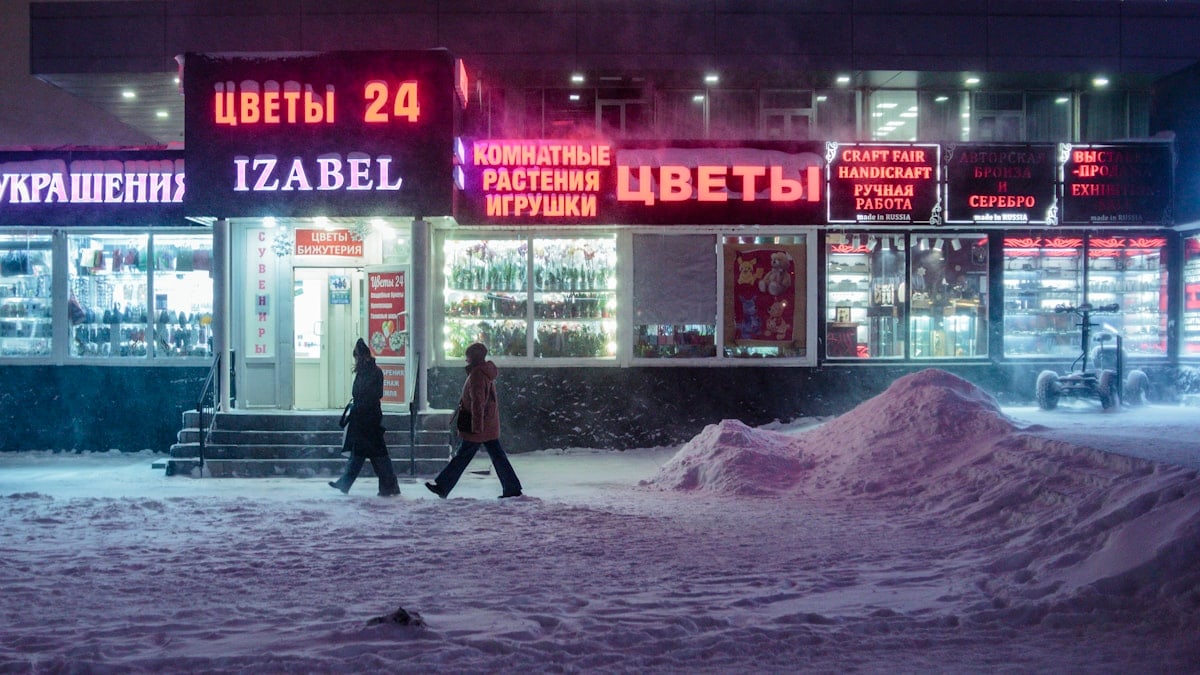 two people walking in the snow in front of a store